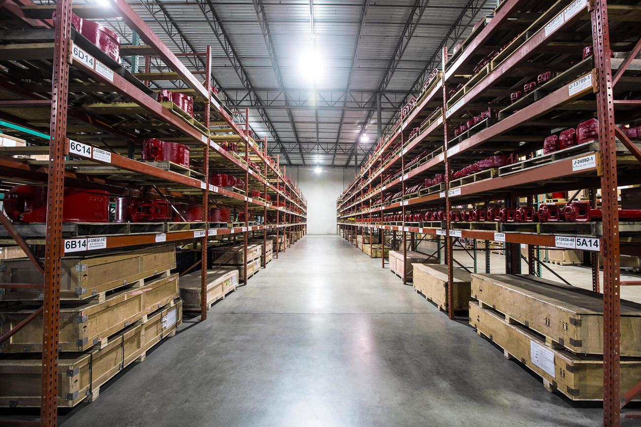 Long Warehouse Aisle with Tall Metal Racks and Red Industrial Components on Shelves