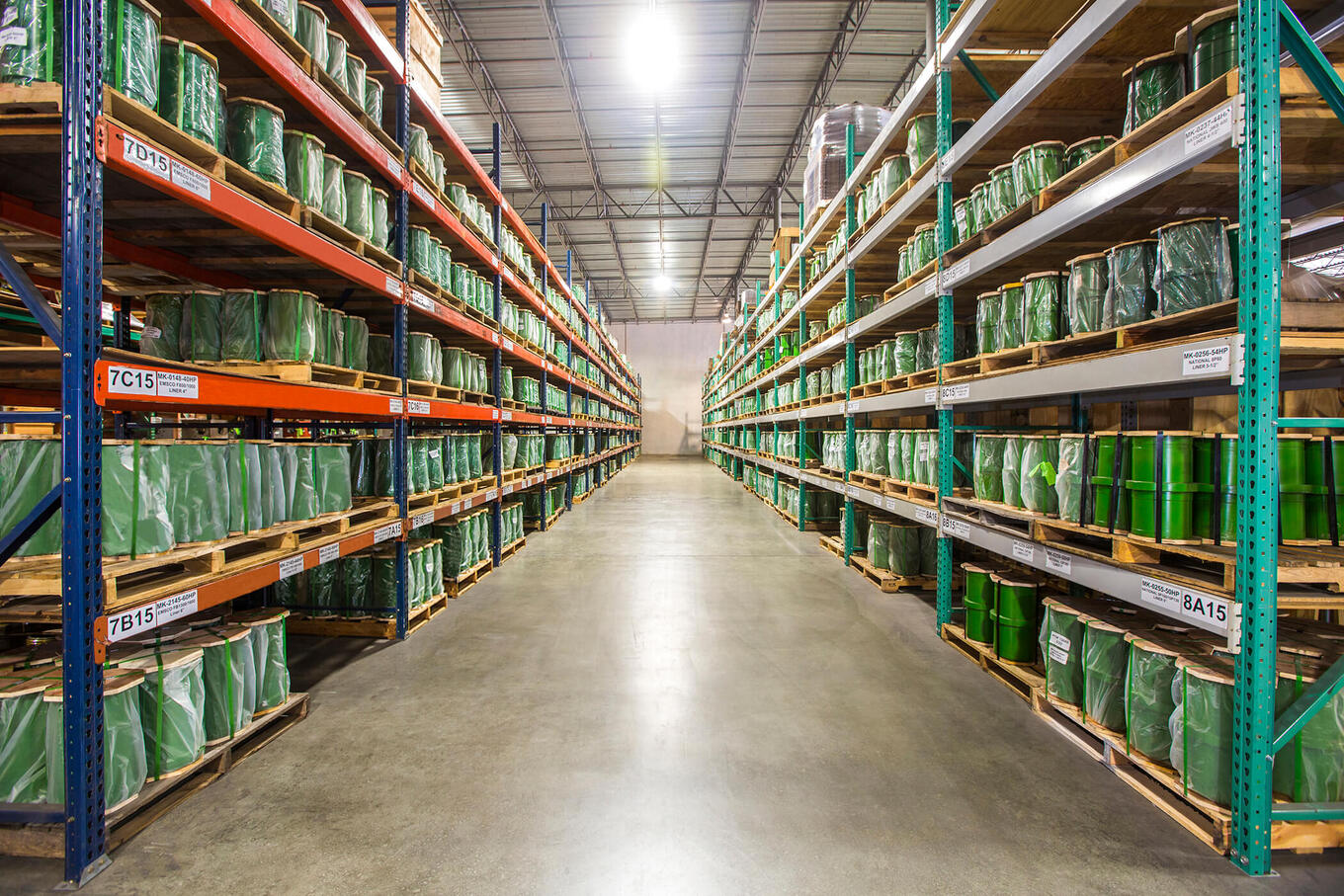 Wide Warehouse Aisle with Tall Metal Shelving on Both Sides Green packaged Pallets Stacked on Wooden Pallets in Neat Rows